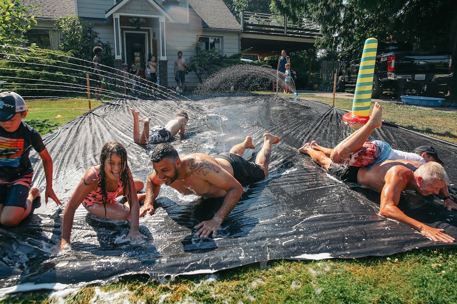 caption: Vasili Vouros, center, and John Cain Jr., right, slip n' slide with their kids in Vouros's front yard on Monday, June 28, 2021, in Skyway. The National Weather Service recorded 108 degrees in SeaTac on Monday, setting an all-time record for the area.