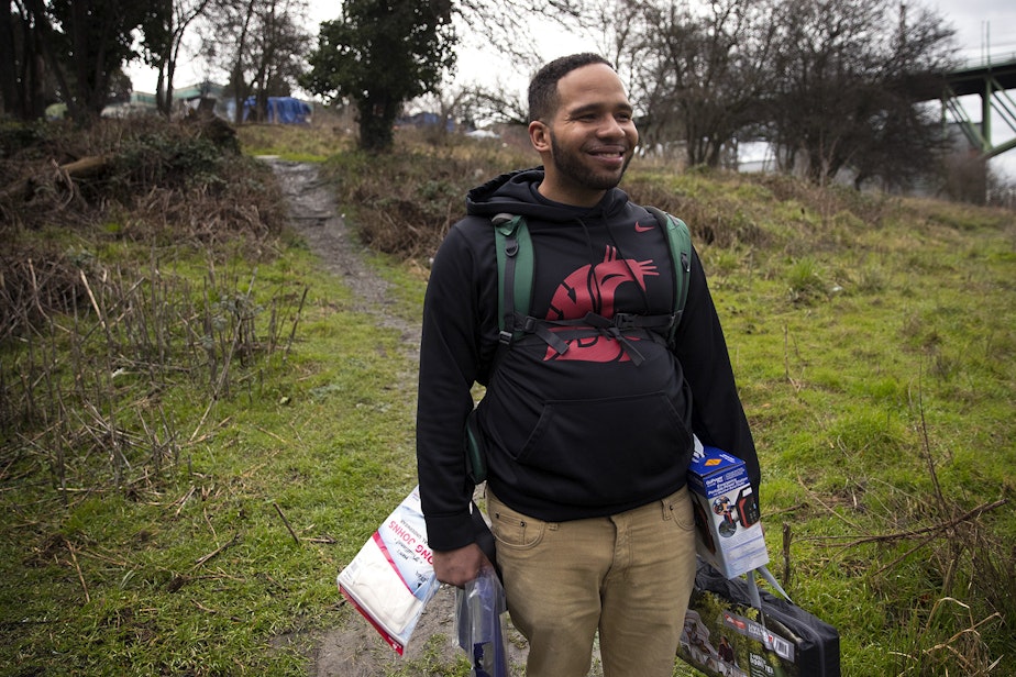 caption: Kalamante Fleeks, 29, smiles while holding mutual aid supplies including long johns, a tarp, a new tent, and a portable power pack delivered to him by Joscelyn and Cass DuVani on Friday, March 5, 2021, in Seattle.