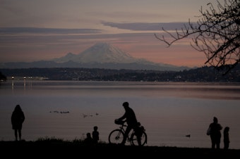 caption: People are silhouetted in the early evening light as they look out at Lake Washington and Mount Rainier at Seward Park, Friday, Nov. 17, 2023, in Seattle.
