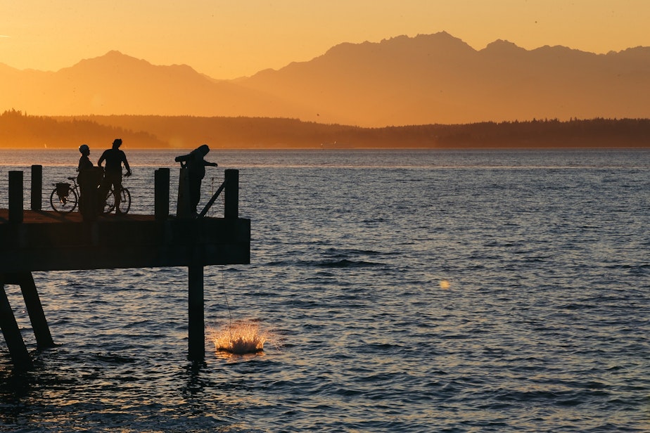 caption: A crab trap splashes down off a pier near Alki Beach as the sun sets, September 1, 2021.