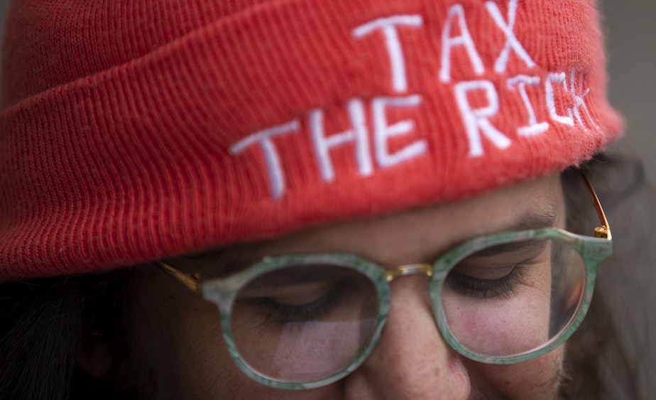 caption: Whitney Kahn attends an "All Together for Seattle Schools" rally wearing a hat that reads "tax the rich" ahead of a school closures meeting on Tuesday, May 28, 2024, at Roosevelt High School in Seattle.