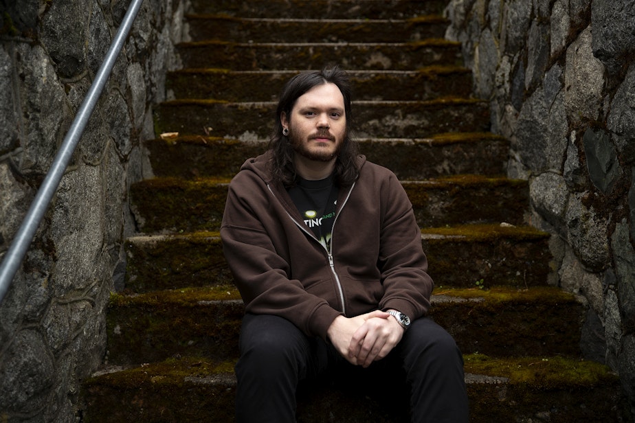 caption: Keenan Calhoun, a 29-year-old grocery clerk at the Lake City Fred Meyer is portrayed on Thursday, April 20, 2023, outside of his home in Seattle.