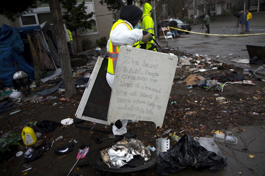 caption: A Seattle Parks and Recreation employee discards a hand written sign that was left behind after unhoused community members were swept from the Ballard Commons Park on Tuesday, December 7, 2021, in Seattle.