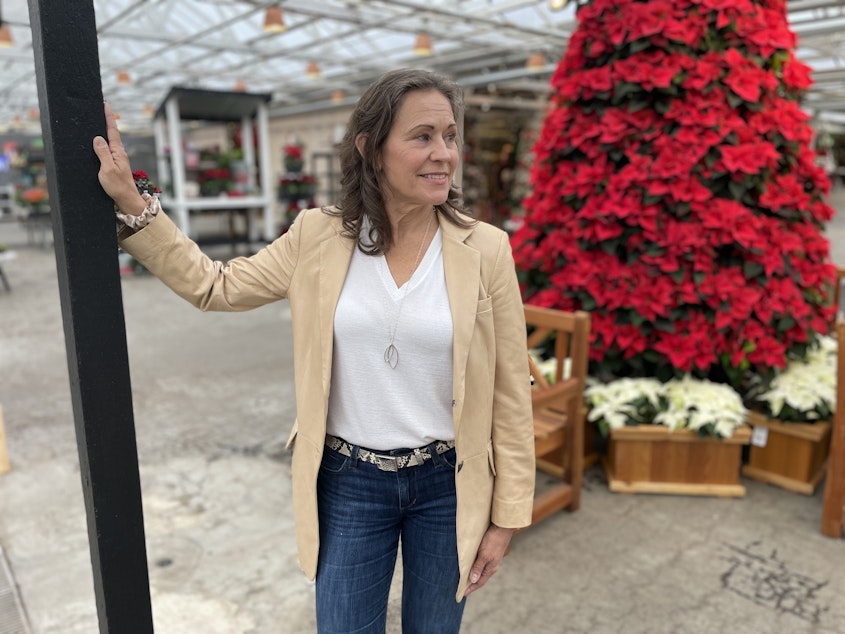 caption: Molbak's CEO Julie Kouhia stands in front of the garden store's poinsettia tree, a hallmark of the store's holiday decorations. After a rift with a developer, the garden and home store opted to close up shop in January 2024.