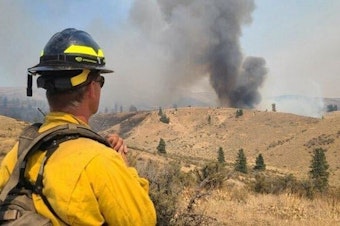 caption: A firefighter looks toward a blaze near Black Canyon, northwest of Yakima. 