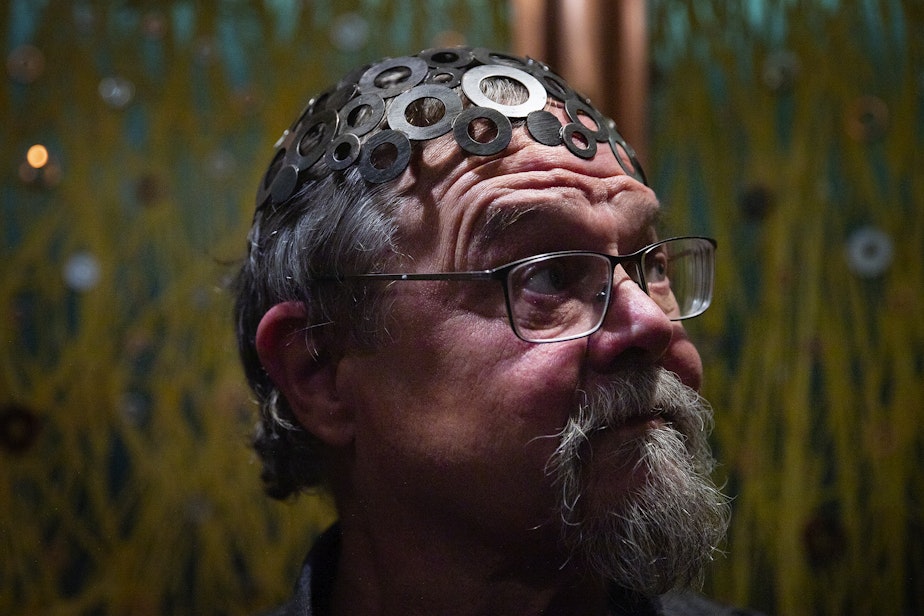 caption: Robert Rudine is shown wearing a hat that he calls the ‘brainwasher,’ aboard his houseboat, the self-declared sovereign nation of Tui Tui, on Tuesday, March 26, 2024, in Seattle.