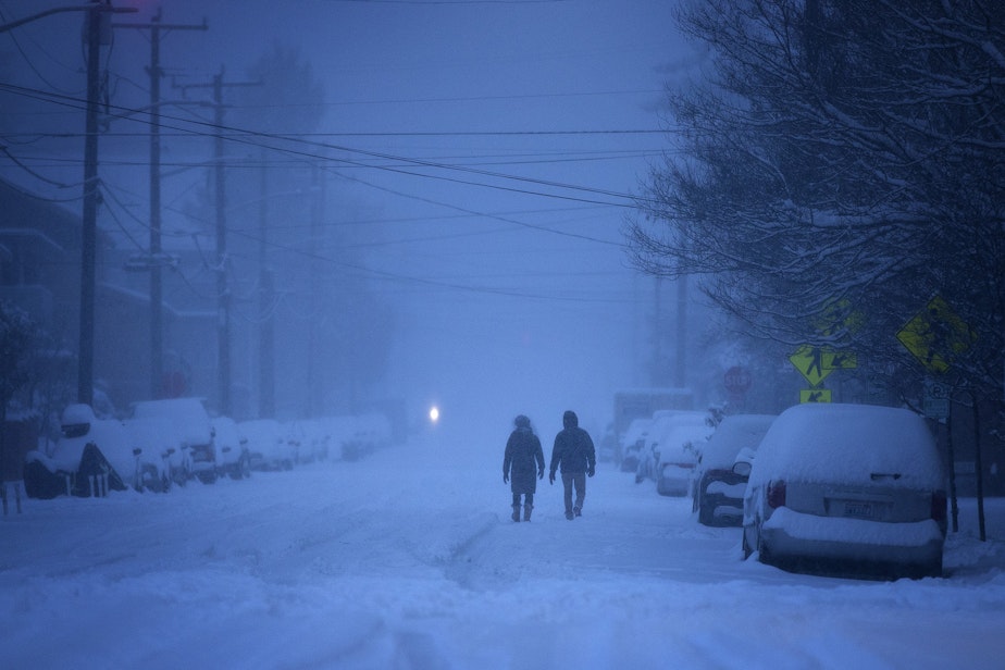 caption: Two people walk through snow as the sun comes up on Saturday, February 13, 2021, along 20th Avenue Northwest near the intersection of NW Market Street in Seattle.